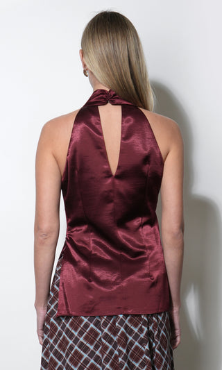 A woman shown from the back wearing a satin halter top in a deep burgundy color, paired with a patterned skirt, against a plain white wall.