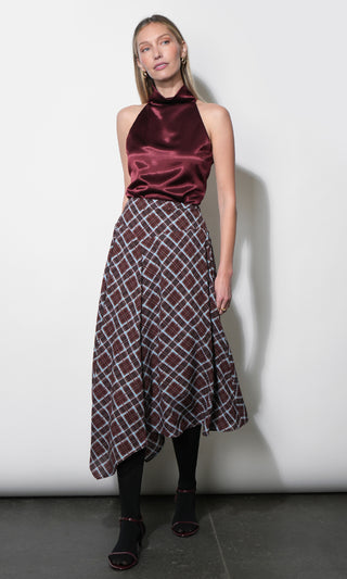 A woman models a sleeveless halter-neck dress featuring a deep burgundy satin bodice and a matching burgundy, black, and white plaid skirt, paired with black tights and black wedge sandals.