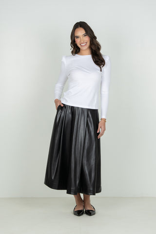 A woman modeling a white long-sleeve top and a black faux-leather midi skirt against a plain light gray studio background.