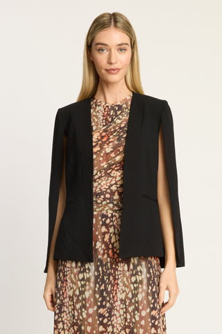 A woman modeling a black sleeveless structured jacket over a brown and beige patterned dress, photographed against a plain light background.