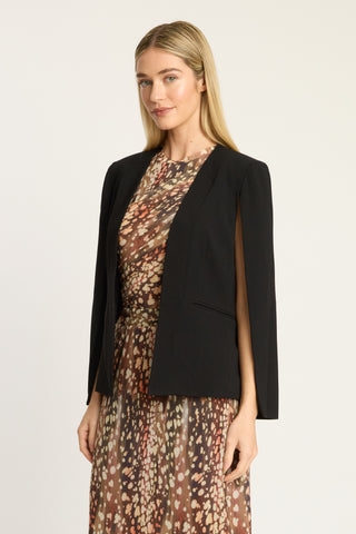 A woman modeling a black open-front blazer over a brown and beige floral print dress, photographed against a clean off-white studio background.