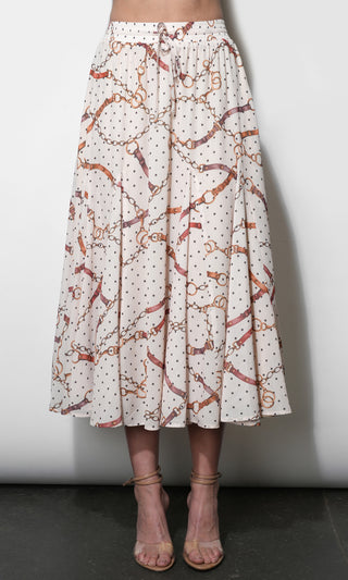 A high-waisted, A-line midi skirt with an allover print of brown horsebit chains and small black polka dots on a cream background, shown on a model wearing beige strappy heels.
