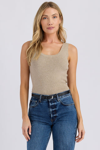 Woman wearing a beige tank top and blue jeans on a white background