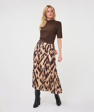 A woman modeling a brown ribbed short-sleeve mock neck top paired with a beige and brown leopard print midi skirt and black ankle boots, set against a plain white studio background.
