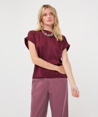 A woman modeling a short-sleeve burgundy top and mauve pinstripe trousers against a plain white studio background.