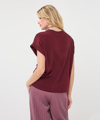 A woman shown from the back wearing a short-sleeve maroon top and mauve pinstriped pants against a plain light gray studio background.