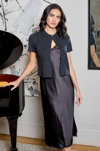 A woman models a dark charcoal gray short-sleeve cropped cardigan with a keyhole cutout over a matching dark gray midi dress, standing next to a black grand piano in a modern room.