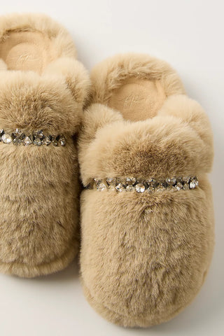 A pair of beige faux fur slip-on slippers decorated with a horizontal row of clear rhinestones across the top, shown against a plain light background.