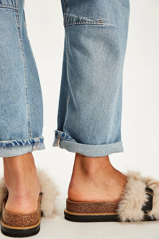 Fluffy beige faux-fur slide sandals with black straps, a gold-tone buckle, and colorful bead accents, paired with cuffed blue jeans.