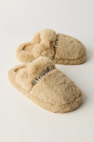 A pair of beige faux fur slippers with a decorative silver rhinestone embellishment across the top, displayed on a clean white background.